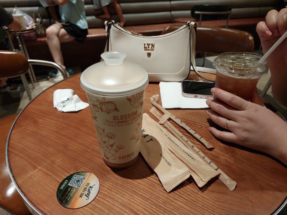 Khám Phá 11 Quán Cafe Đội Cấn Tuyệt Vời Cho Thư Giãn Và Làm Việc 22 Hai ly trà trên bàn gỗ, kèm theo túi xách trắng và điện thoại di động.