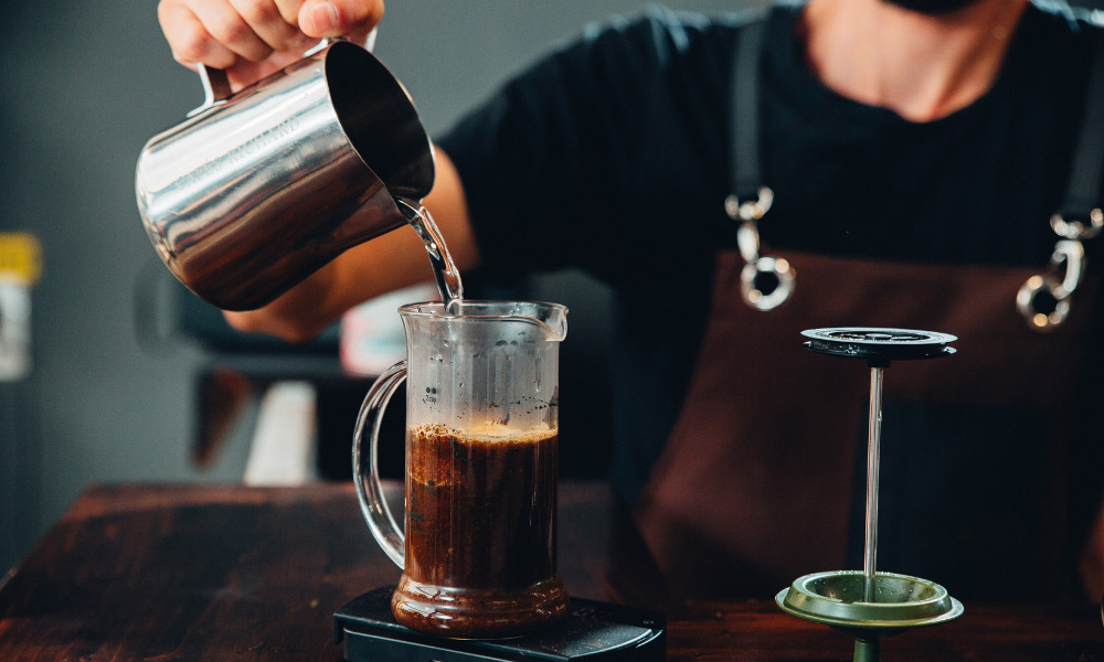 Khám Phá 14 Quán Cafe Hồ Tùng Mậu: Điểm Chill Lý Tưởng Tại Cầu Giấy 22 Người đang rót nước vào bình pha cà phê trên bàn gỗ, với dụng cụ pha chế bên cạnh.