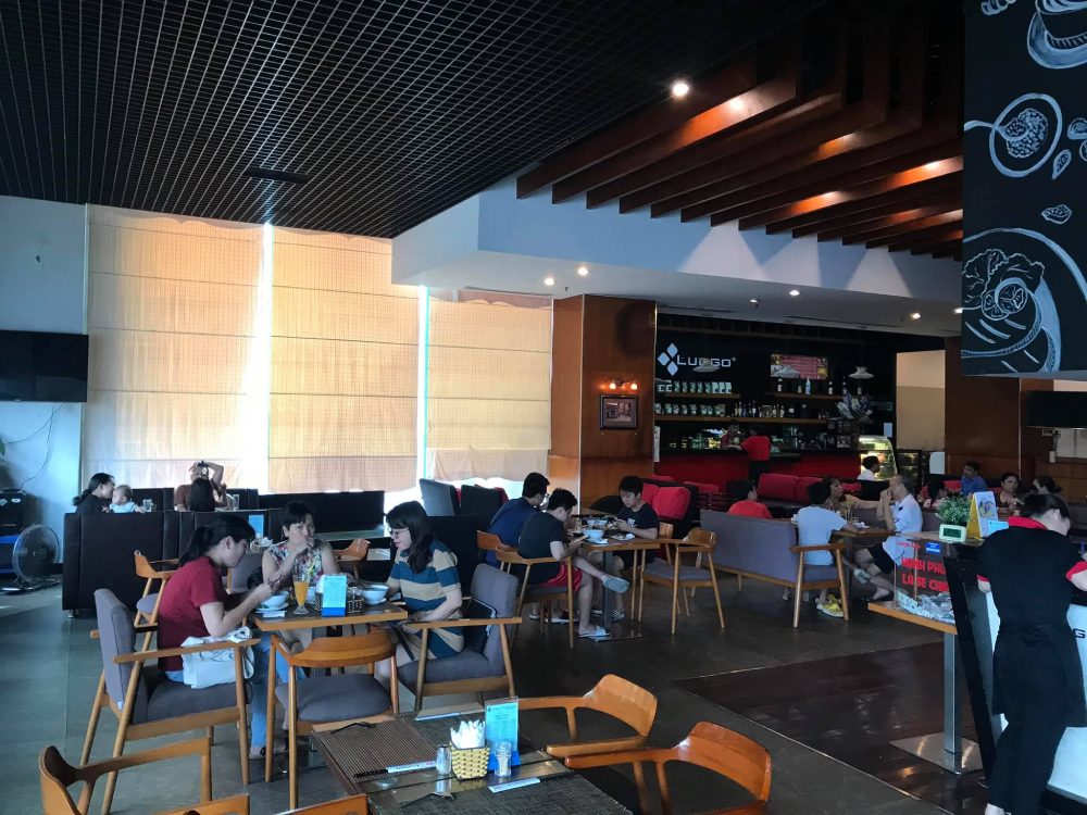 Khám Phá 7 Quán Cafe Tuyệt Đẹp Ở Ngã Tư Sở: View Đẹp, Đồ Uống Ngon, Giá Phải Chăng 21 Quán cà phê đông khách đang ngồi trò chuyện và thưởng thức đồ uống, nội thất hiện đại và ánh sáng tự nhiên.