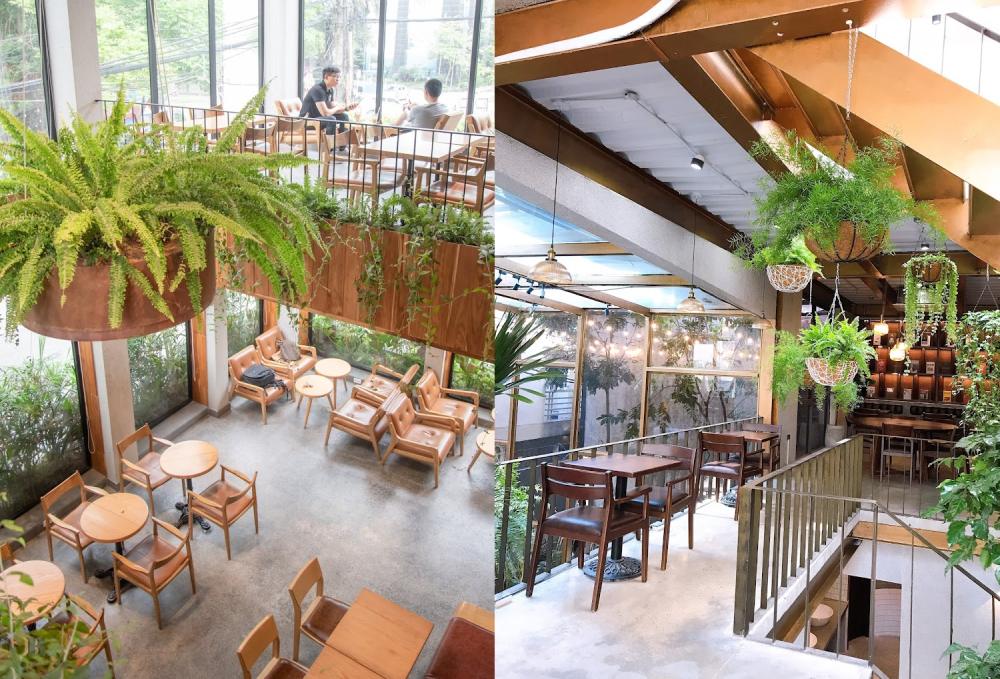 Khám Phá 7 Quán Cafe Tuyệt Đẹp Ở Ngã Tư Sở: View Đẹp, Đồ Uống Ngon, Giá Phải Chăng 9 Quán cà phê hai tầng với nhiều cây xanh, bàn ghế gỗ, ánh sáng tự nhiên từ cửa kính lớn.