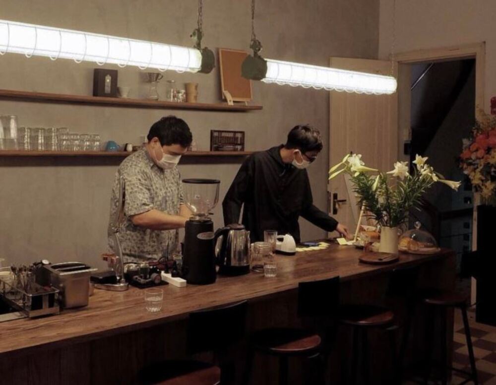 Khám Phá 9 Quán Cafe Độc Đáo Trên Đường Hoàng Hoa Thám 18 Hai người đang chuẩn bị đồ uống tại quầy bar, xung quanh có hoa và dụng cụ pha chế.