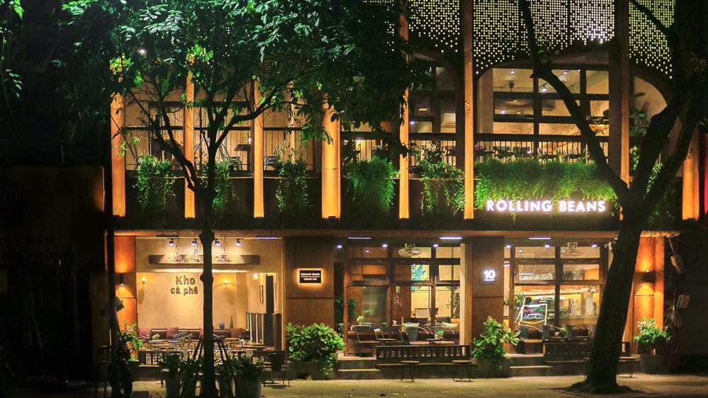 15 Quán Cafe Chùa Láng Với Không Gian Thư Giãn Tuyệt Đẹp 8 Mặt tiền quán cà phê vào buổi tối với ánh sáng ấm áp, cây xanh và cửa kính lớn.
