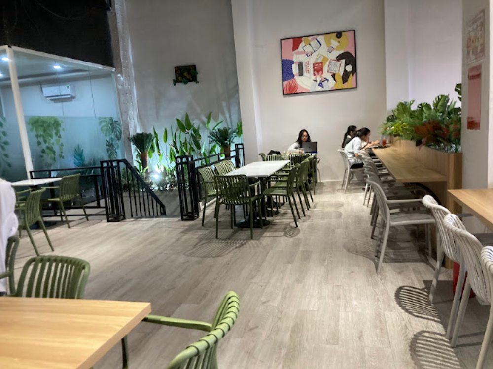 Khám Phá Top 6 Quán Cafe Mở Cửa 24h Tại Quận 3 Cho Người Yêu Thích Cú Đêm 19 Quán cà phê với bàn ghế hiện đại, cây xanh trang trí và tranh treo tường; vài người đang ngồi làm việc.