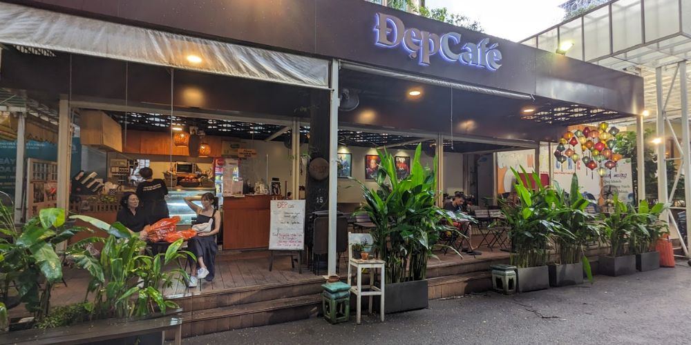 Khám Phá Top Quán Cafe Sách Hot Nhất Quận 1 Bạn Không Thể Bỏ Lỡ Năm Nay 13 Mặt tiền quán cà phê với biển hiệu "ĐẹpCafé", có chỗ ngồi ngoài trời và cây xanh trang trí phía trước.