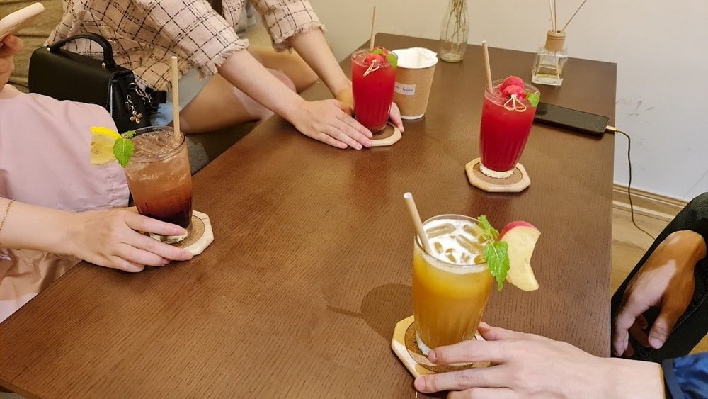 Khám Phá 10+ Quán Cafe Đẹp Ở Đặng Văn Ngữ: Đồ Uống Ngon, Giá Cả Hấp Dẫn 6 Bàn gỗ với bốn ly nước trái cây nhiều màu sắc, mỗi ly có ống hút và lá bạc hà trang trí.