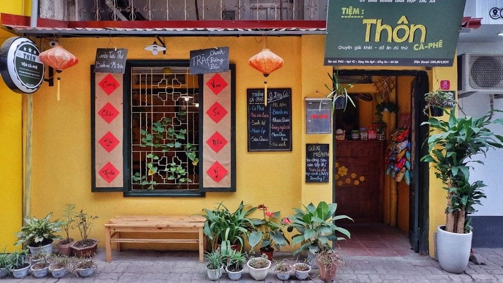 Khám Phá 10+ Quán Cafe Đẹp Ở Đặng Văn Ngữ: Đồ Uống Ngon, Giá Cả Hấp Dẫn 25 Mặt tiền quán cà phê nhỏ với tường vàng, cửa sổ trang trí và bảng hiệu ghi tên quán cùng thực đơn đồ uống.