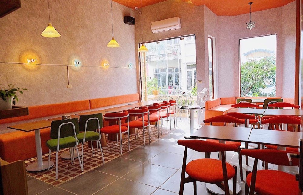 Khám Phá 12+ Quán Cafe Đẹp Ở Tây Sơn Với Đồ Uống Ngon 16 Quán cà phê với bàn ghế đỏ và xanh, ánh sáng dịu nhẹ, cửa sổ lớn nhìn ra ngoài phố.