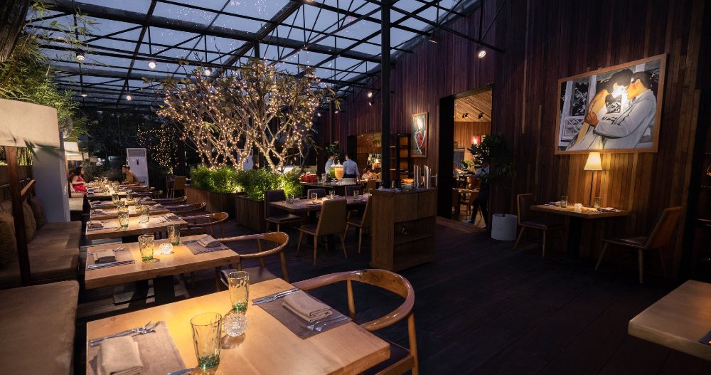 Khám Phá Top 10 Quán Rooftop Quận 1: View Đẹp Ngắm Thành Phố, Trải Nghiệm Thư Giãn Tuyệt Đỉnh 6 Nhà hàng với ánh đèn ấm áp, bàn ghế gỗ, cây xanh trang trí và bức tranh treo tường.