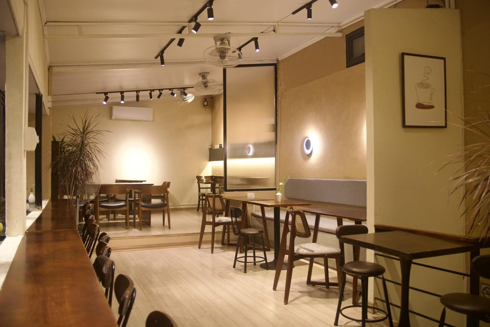 15 Quán Cafe Chùa Láng Với Không Gian Thư Giãn Tuyệt Đẹp 6 Quán cà phê với nội thất gỗ, ánh sáng dịu, tranh treo tường và bàn ghế gỗ, không gian ấm cúng và hiện đại.