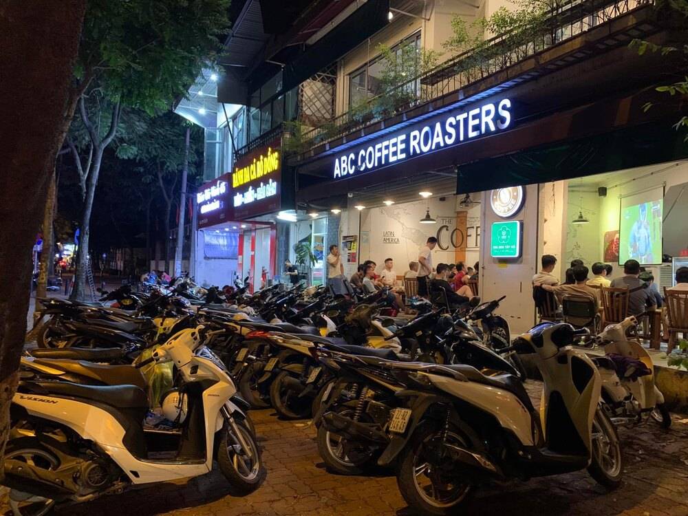 Khám Phá 10+ Quán Cafe Đẹp Ở Đặng Văn Ngữ: Đồ Uống Ngon, Giá Cả Hấp Dẫn 17 Quán cà phê ban đêm với nhiều xe máy đậu phía trước, khách ngồi bên trong xem màn hình lớn.