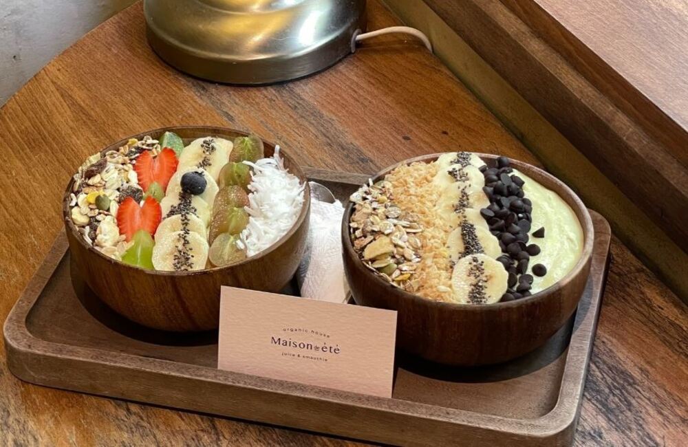 Khám Phá 10+ Quán Cafe Đẹp Ở Đặng Văn Ngữ: Đồ Uống Ngon, Giá Cả Hấp Dẫn 20 Hai tô sinh tố trái cây, trang trí với chuối, dâu, nho, hạt và socola, đặt trên khay gỗ cạnh cửa sổ.