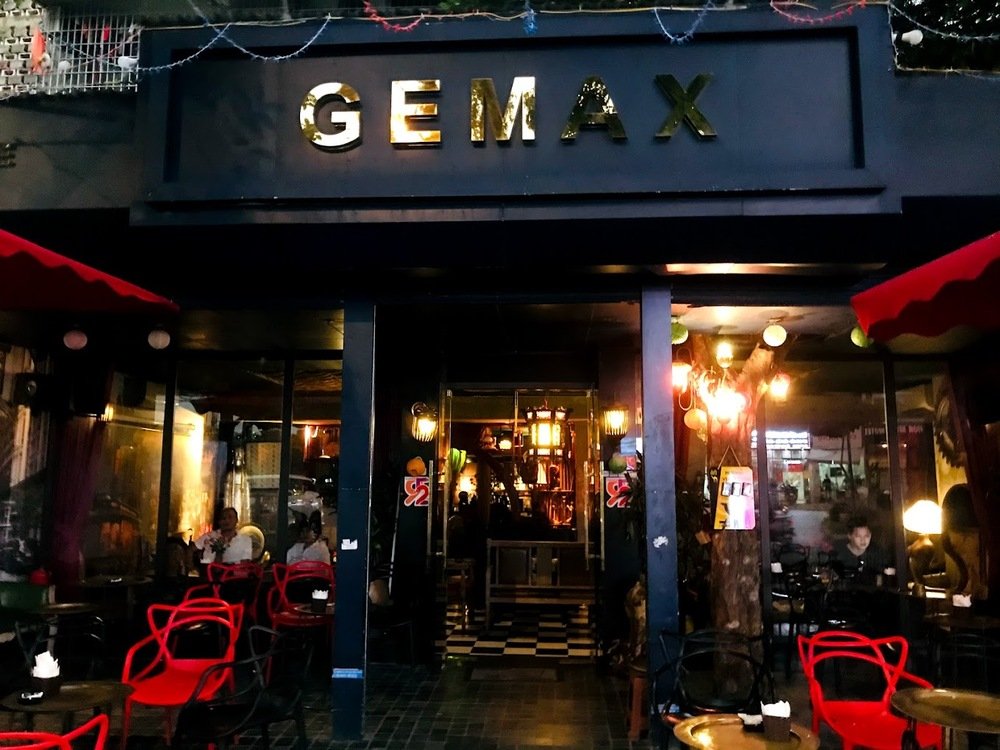 Khám Phá 10+ Quán Cafe Đẹp Ở Đặng Văn Ngữ: Đồ Uống Ngon, Giá Cả Hấp Dẫn 15 Mặt tiền quán cà phê với bảng hiệu "GEMAX", ghế đỏ và đèn trang trí, không gian tối giản và ấm cúng.