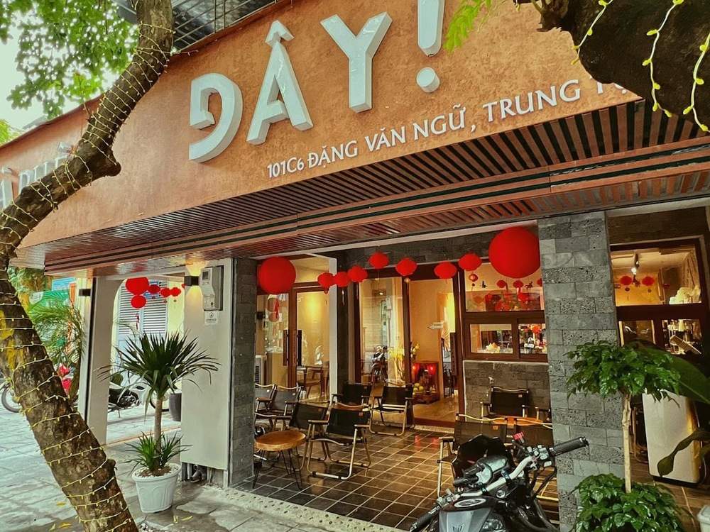 Khám Phá 10+ Quán Cafe Đẹp Ở Đặng Văn Ngữ: Đồ Uống Ngon, Giá Cả Hấp Dẫn 23 Mặt tiền quán cà phê với biển hiệu lớn, trang trí đèn lồng đỏ, cây xanh và xe máy đậu trước cửa.