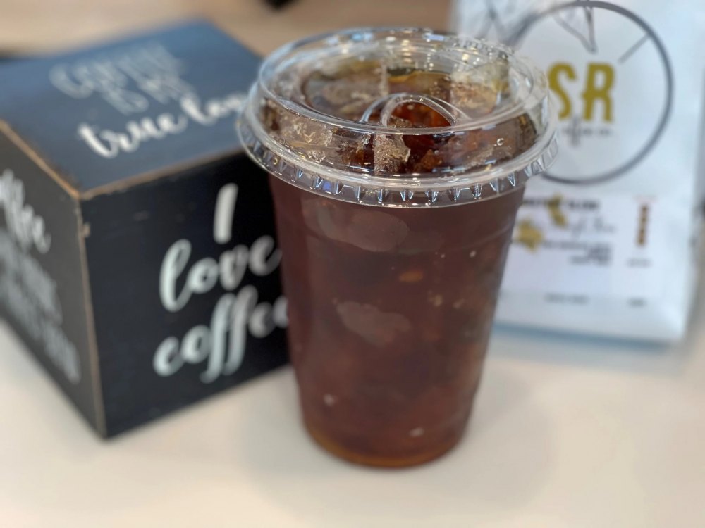 americano-da Ly cà phê đá trong cốc nhựa, bên cạnh là hộp và túi đựng, có chữ "I love coffee".