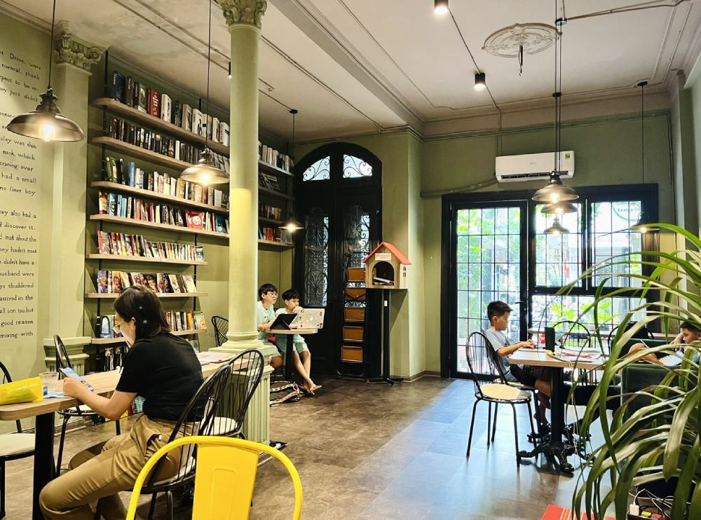 Khám Phá 11 Quán Cafe Sách Độc Đáo Tại Cầu Giấy Hút Hồn Độc Giả 11 Quán cà phê yên tĩnh với nhiều sách trên kệ, có người đang ngồi đọc và làm việc tại các bàn.