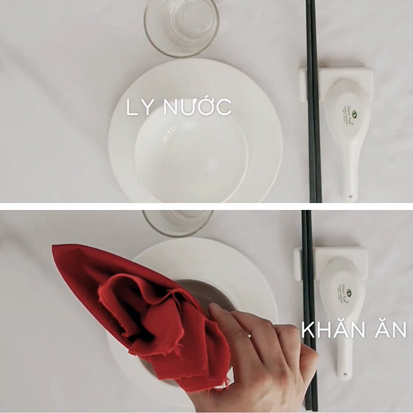 Bàn ăn với ly nước, đĩa, bát, đũa và khăn ăn đỏ được sắp xếp gọn gàng trên nền trắng.