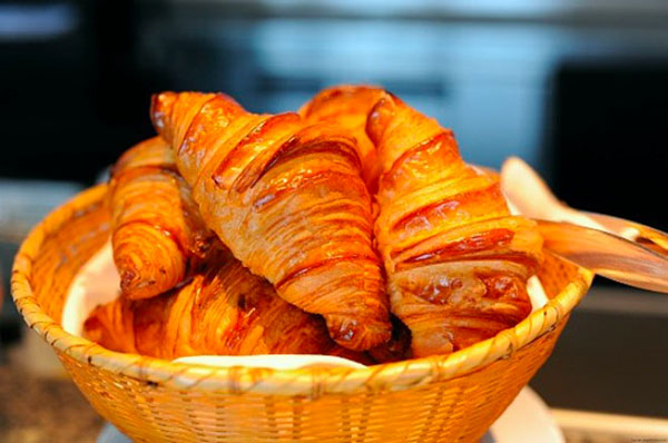 Giỏ bánh croissant tươi ngon, vàng óng, đặt trên bàn với phông nền mờ.