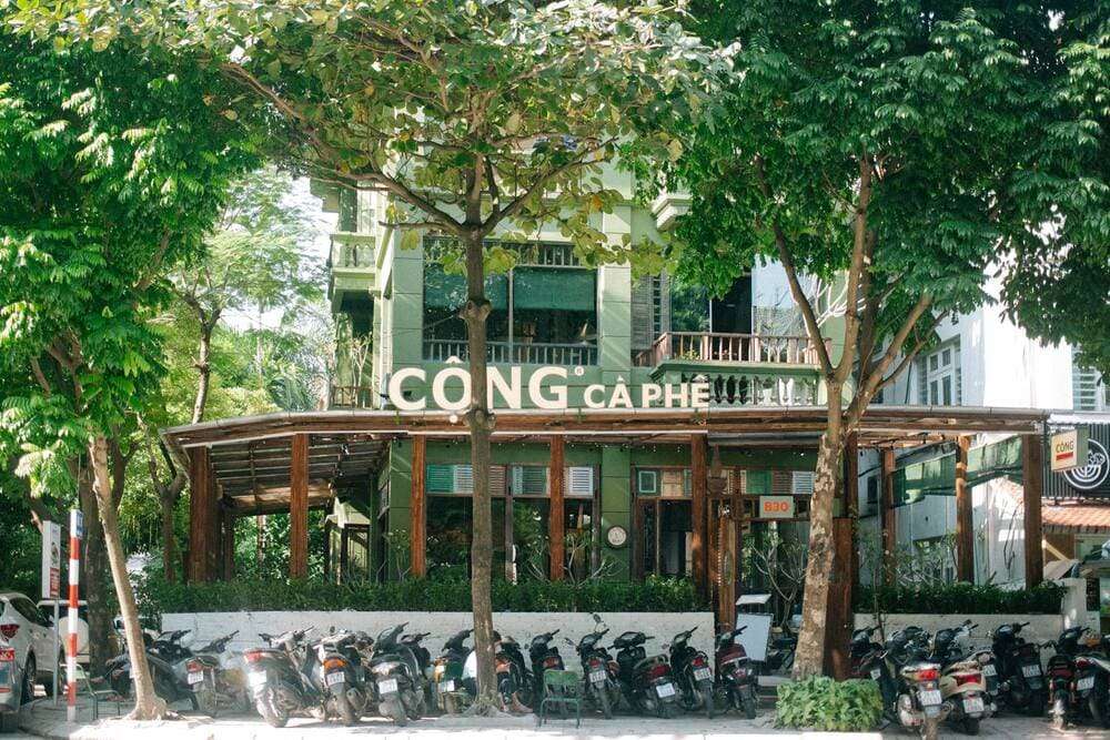 Khám Phá 15 Quán Cafe Hấp Dẫn Trên Đường Nguyễn Thị Định 9 Quán cà phê màu xanh lá cây với hàng xe máy đỗ phía trước, xung quanh có nhiều cây xanh tươi tốt.