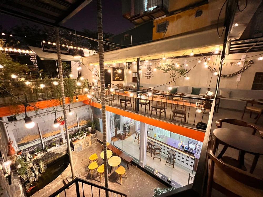 Khám Phá 10+ Quán Cafe Đẹp Ở Đặng Văn Ngữ: Đồ Uống Ngon, Giá Cả Hấp Dẫn 24 Quán cà phê hai tầng vào buổi tối, trang trí đèn dây, bàn ghế gỗ, không gian ấm cúng.
