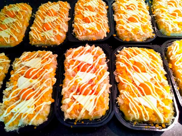 Các khay bánh mì ngọt phủ sốt mayonnaise, trứng và ruốc, được xếp gọn gàng trên bề mặt.