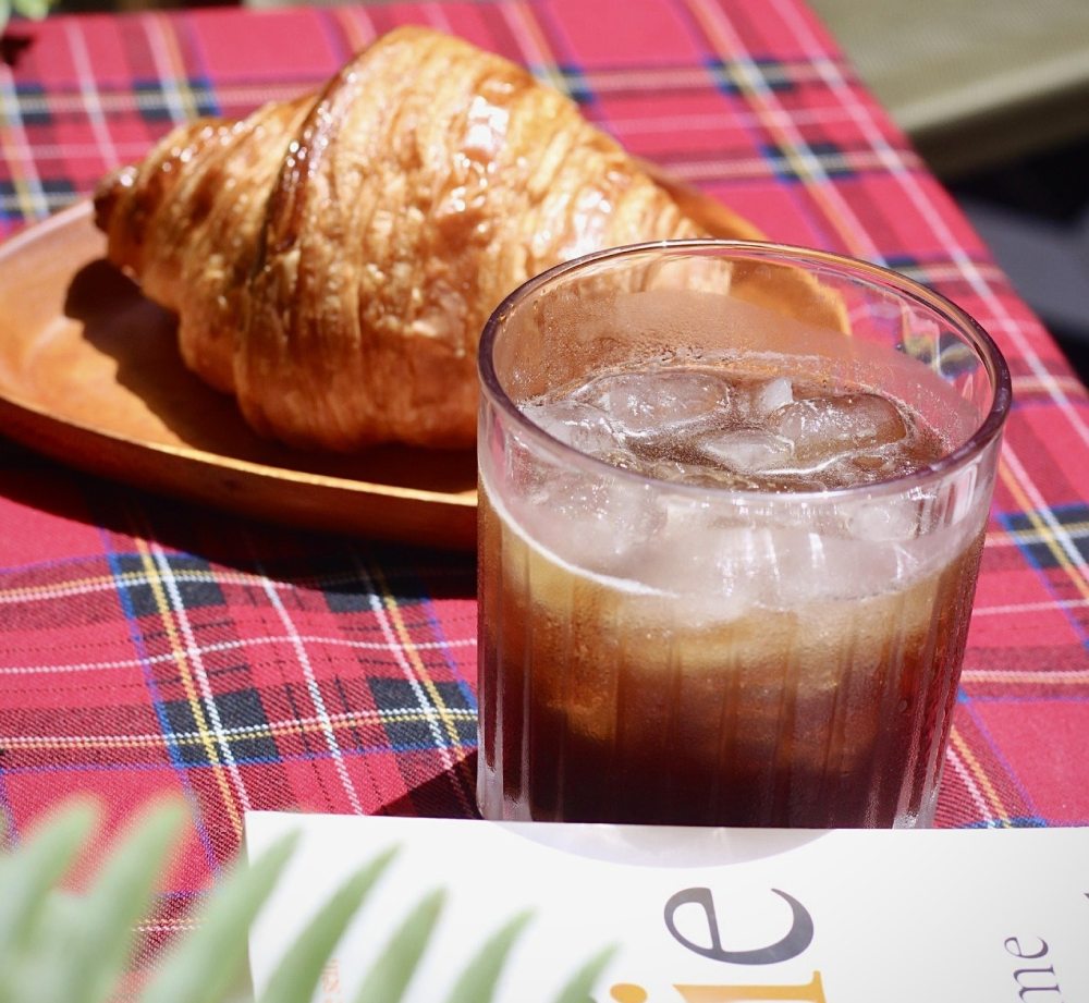 Khám Phá 11 Quán Cafe Sách Độc Đáo Tại Cầu Giấy Hút Hồn Độc Giả 12 Ly cà phê đá và bánh croissant trên bàn trải khăn kẻ caro đỏ.