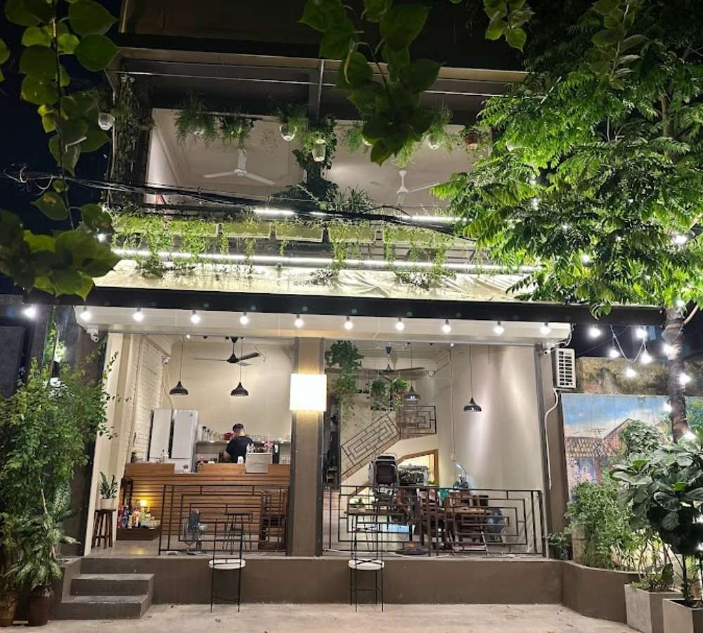 Khám Phá Top Quán Cafe Đẹp Ở Liễu Giai: Đồ Uống Ngon, Không Gian Thư Giãn 11 Quán cà phê hai tầng với ánh đèn lung linh, cây xanh trang trí, bàn ghế ngoài trời, và không gian mở.