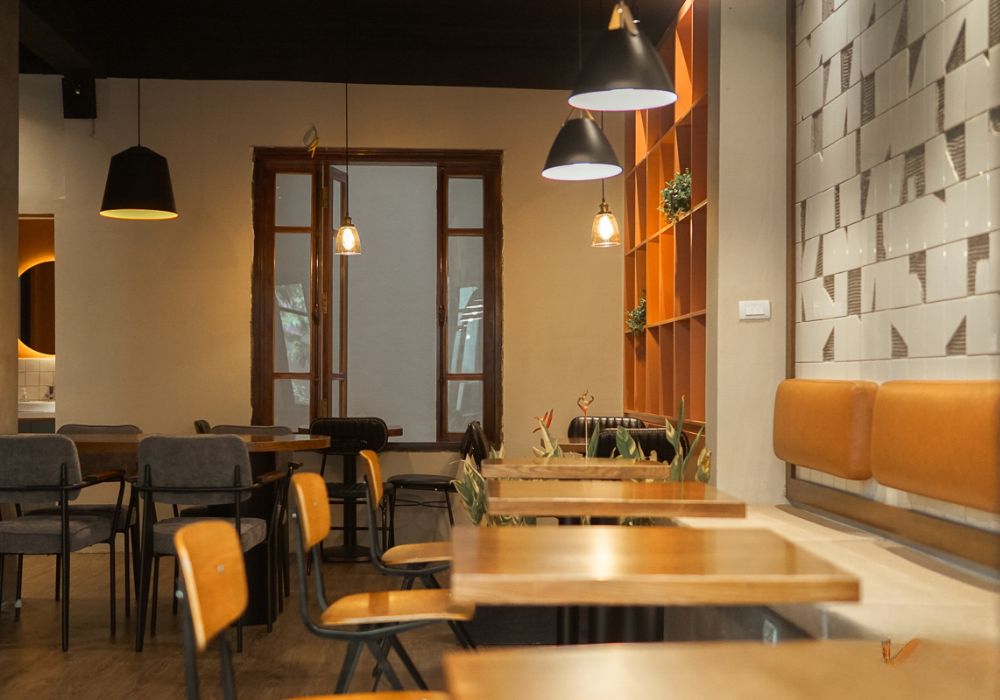 Khám Phá Top 10 Quán Cafe Láng Hạ: View Đẹp, Menu Hấp Dẫn, Giá Cực Hợp Lý 12 Quán cà phê với bàn ghế gỗ, đèn treo và kệ trang trí, mang phong cách hiện đại và ấm cúng.