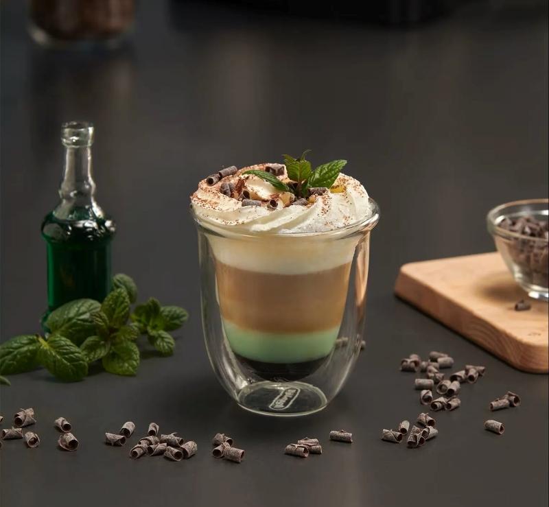 Ly c&agrave; ph&ecirc; với lớp kem v&agrave; bạc h&agrave;, b&ecirc;n cạnh l&agrave; l&aacute; bạc h&agrave;, vụn s&ocirc; c&ocirc; la v&agrave; chai nhỏ tr&ecirc;n nền b&agrave;n tối m&agrave;u.