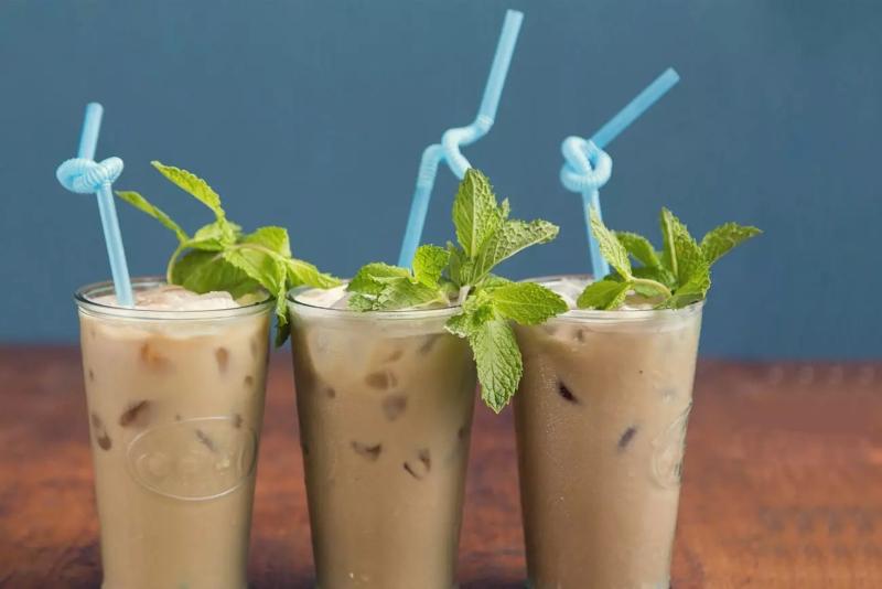 Ba ly c&agrave; ph&ecirc; sữa đ&aacute; với ống h&uacute;t xanh v&agrave; l&aacute; bạc h&agrave; trang tr&iacute; tr&ecirc;n mặt b&agrave;n gỗ.