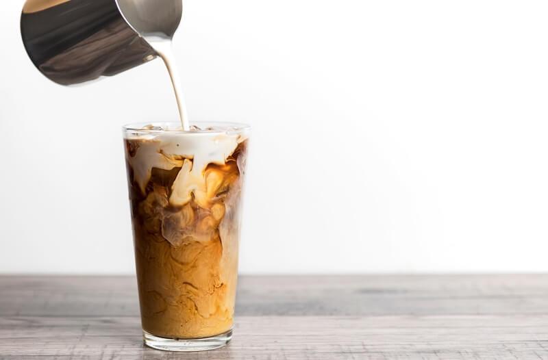 Ly cà phê sữa đá với sữa đang được rót vào, tạo nên các lớp màu sắc hòa quyện.