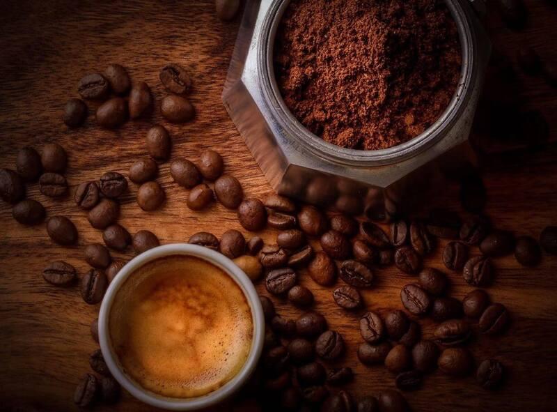 Tách cà phê espresso bên cạnh bình cà phê và hạt cà phê trên nền gỗ.