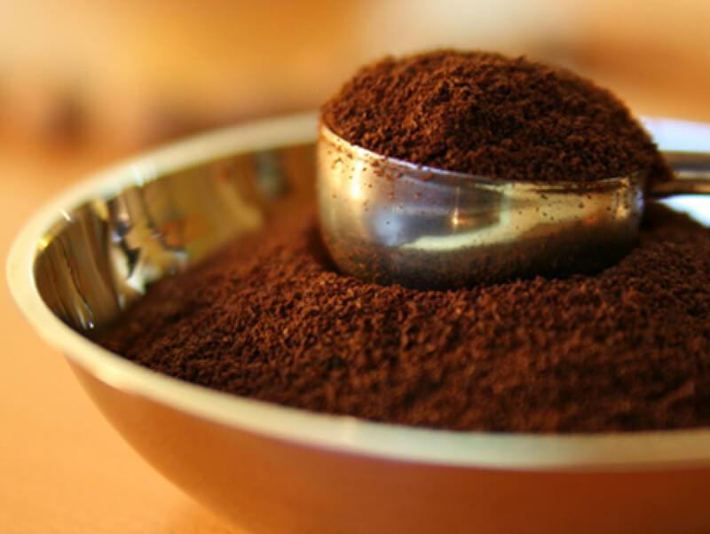 Muỗng kim loại chứa đầy bột cà phê màu nâu, đặt trong một chiếc bát.