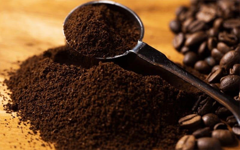 Một thìa bột cà phê bên cạnh những hạt cà phê trên bề mặt gỗ.