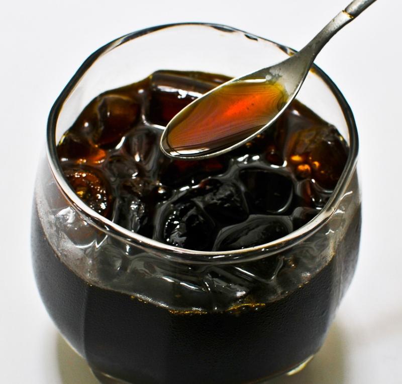 Ly nước đ&aacute; lạnh m&agrave;u n&acirc;u sẫm, với th&igrave;a kim loại đựng chất lỏng m&agrave;u n&acirc;u đỏ ph&iacute;a tr&ecirc;n.