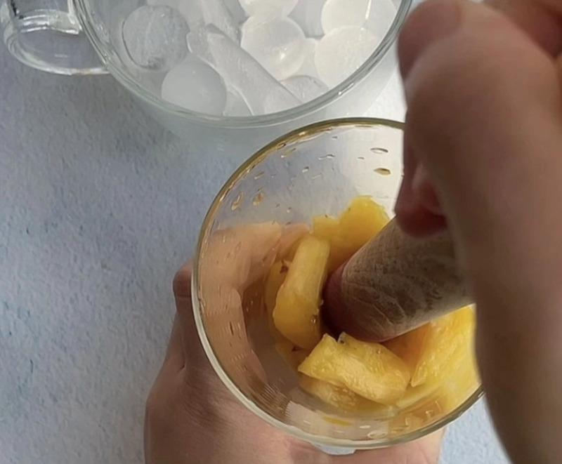 Người đang nghiền n&aacute;t dứa trong cốc thủy tinh, b&ecirc;n cạnh l&agrave; cốc đ&aacute; vi&ecirc;n.