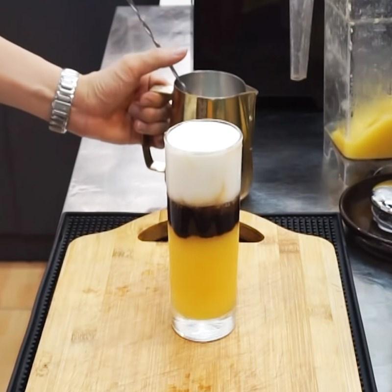 Ly nước ba tầng m&agrave;u v&agrave;ng, đen, trắng được đặt tr&ecirc;n thớt gỗ, người cầm b&igrave;nh kim loại ph&iacute;a sau.