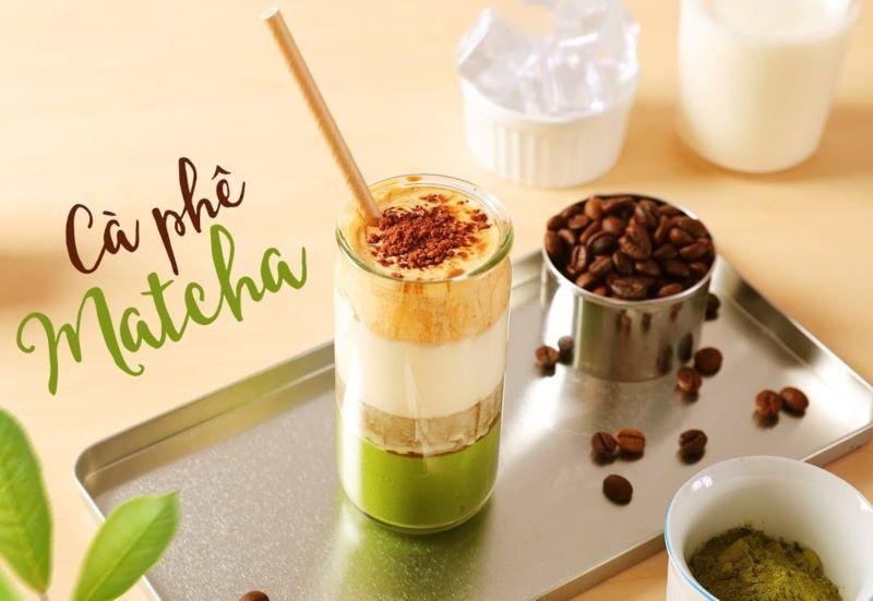 Ly c&agrave; ph&ecirc; matcha tr&ecirc;n khay, b&ecirc;n cạnh l&agrave; hạt c&agrave; ph&ecirc; v&agrave; bột matcha trong b&aacute;t nhỏ.
