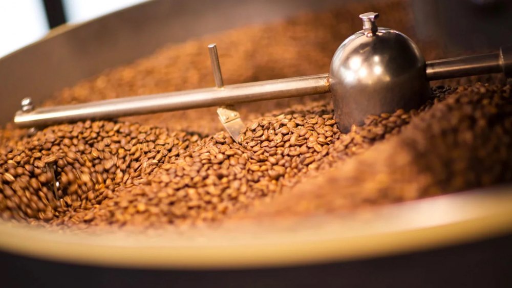 Hạt cà phê đang được rang trong máy rang lớn với cánh khuấy kim loại.