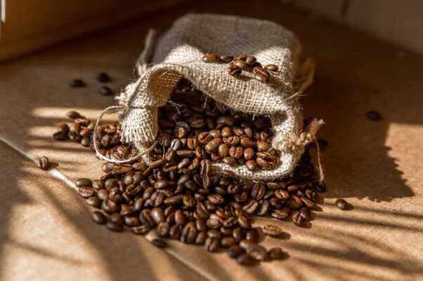 Hạt cà phê rơi khỏi túi vải trên nền giấy, ánh sáng chiếu vào tạo bóng.