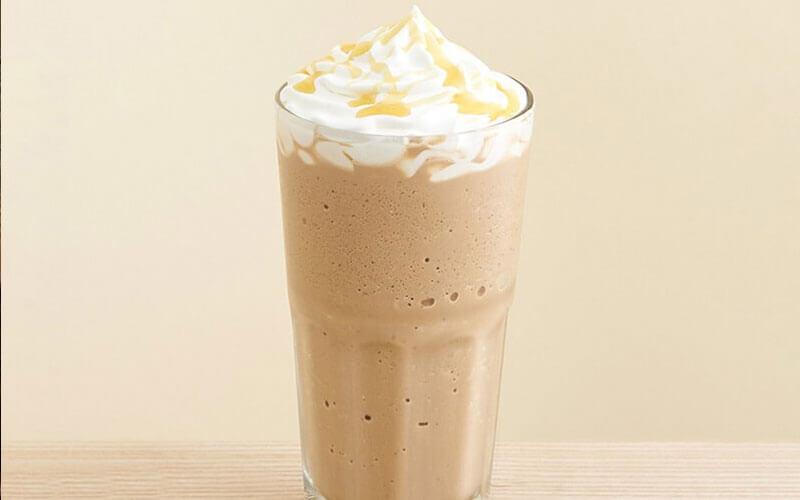 Ly c&agrave; ph&ecirc; đ&aacute; xay với kem tươi v&agrave; sốt caramel, đặt tr&ecirc;n mặt b&agrave;n gỗ, nền m&agrave;u be nhạt.