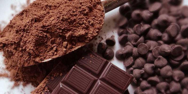 Bột cacao trong th&igrave;a, thanh s&ocirc;-c&ocirc;-la vu&ocirc;ng v&agrave; s&ocirc;-c&ocirc;-la chip tr&ecirc;n bề mặt trắng.