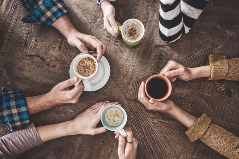 Năm người ngồi quanh b&agrave;n gỗ, mỗi người cầm một t&aacute;ch c&agrave; ph&ecirc; với nhiều loại kh&aacute;c nhau.