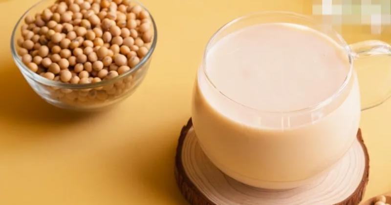 Ly sữa đậu n&agrave;nh b&ecirc;n cạnh b&aacute;t đậu n&agrave;nh, đặt tr&ecirc;n nền m&agrave;u v&agrave;ng.