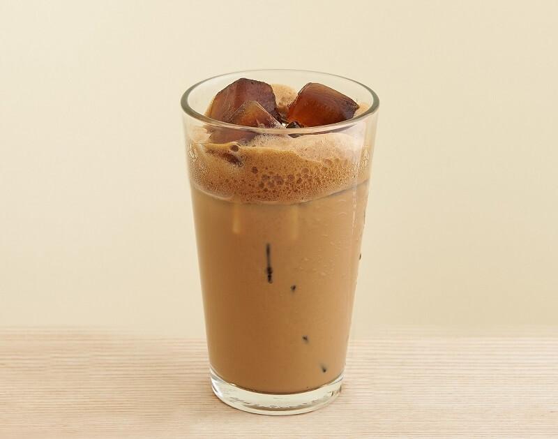 Ly c&agrave; ph&ecirc; sữa đ&aacute; với bọt nhẹ tr&ecirc;n bề mặt, đặt tr&ecirc;n b&agrave;n gỗ s&aacute;ng m&agrave;u.