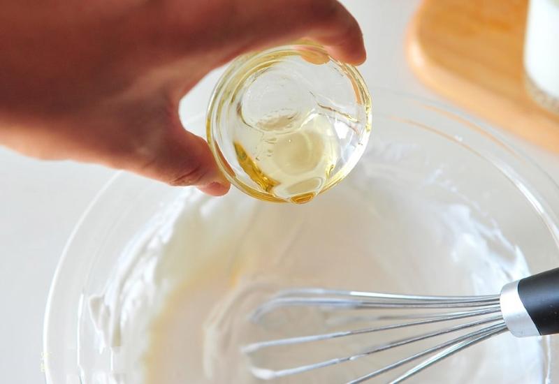 Tay cầm ch&eacute;n nhỏ đổ chất lỏng m&agrave;u v&agrave;ng v&agrave;o t&ocirc; c&oacute; phới lồng, nền bếp s&aacute;ng.