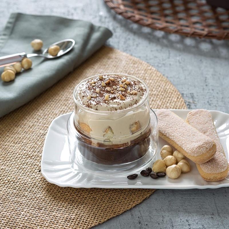 Ly tiramisu với b&aacute;nh quy, hạt phỉ v&agrave; hạt c&agrave; ph&ecirc; tr&ecirc;n đĩa trắng, nền trải b&agrave;n bằng d&acirc;y c&oacute;i.