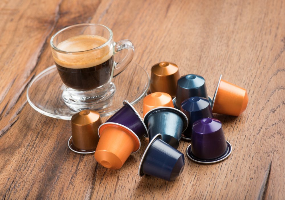 ca-phe-vien-nen-la-gi Ly cà phê espresso trong suốt bên cạnh nhiều viên nén cà phê màu sắc trên bàn gỗ.