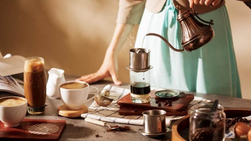 Người pha chế cà phê phin trên bàn với nhiều ly cà phê và dụng cụ pha chế xung quanh.