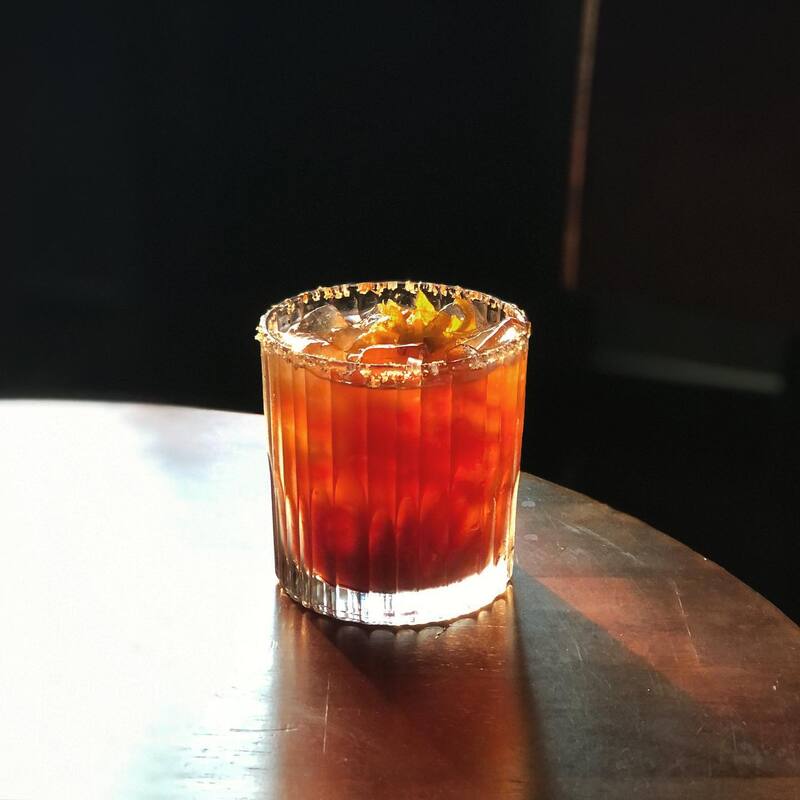 Ly cocktail màu cam đặt trên bàn gỗ, có muối trên miệng ly và vài lát trang trí bên trong.