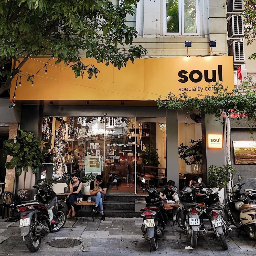 Quán cà phê với biển hiệu "soul" màu vàng, có xe máy đỗ trước cửa và khách ngồi uống cà phê bên ngoài.